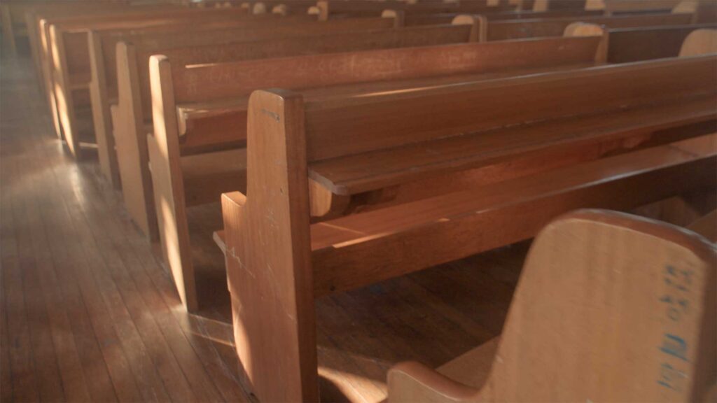 Empty wooden church benches illuminated by soft daylight, evoking collective rituals and social discipline during Korea’s industrial era