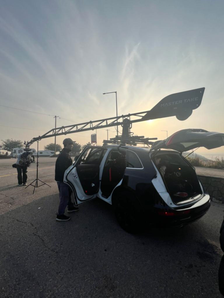 A camera car with a roof-mounted crane arm and stabilized rig prepared for a vehicle tracking shot during an on-location film shoot at dusk.