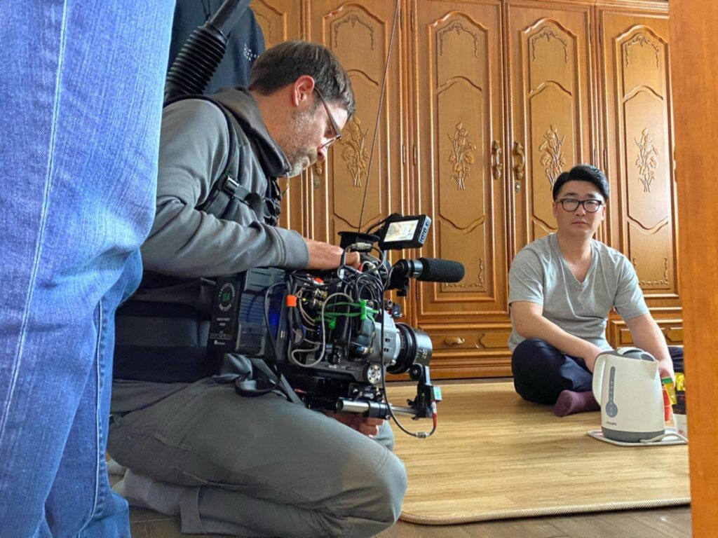 Cinematographer filming an interview in a private Seoul apartment with a compact crew and minimal equipment