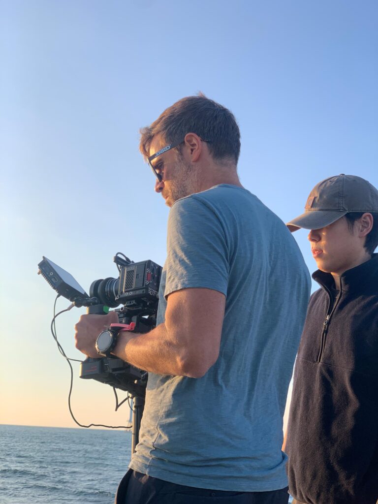 Cinematographer reviewing camera settings with a small crew during an outdoor shoot by the sea in South Korea