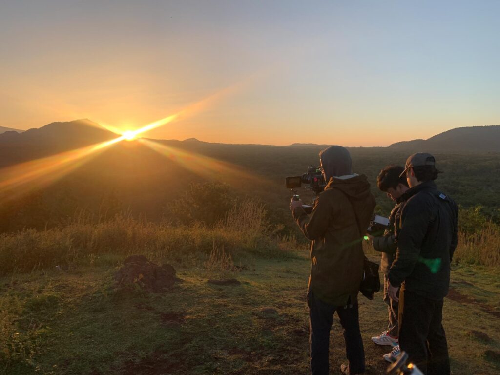Small film crew capturing a sunset landscape during an outdoor shoot in South Korea, focusing on light and timing