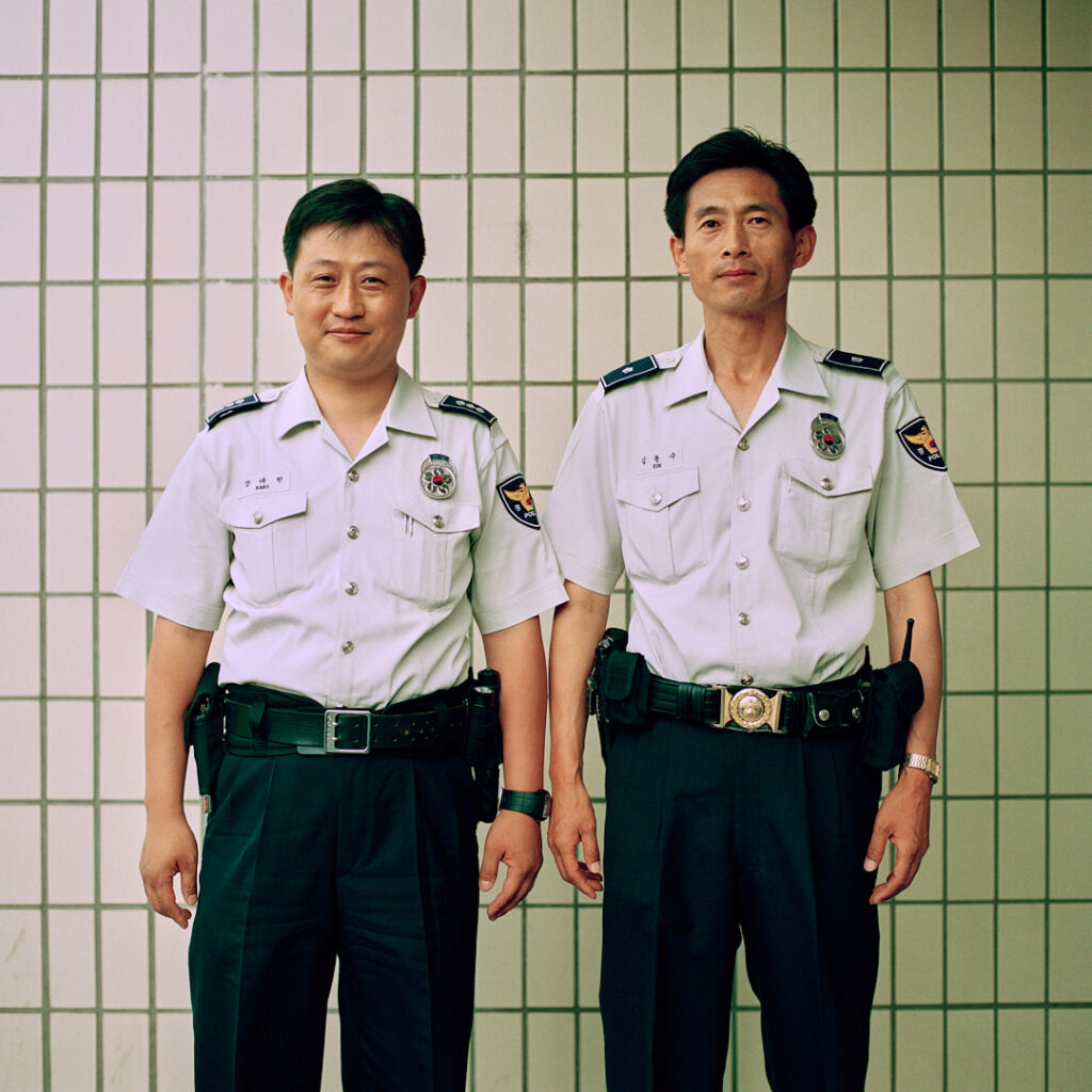 Identically dressed police officers stand before a tiled wall in Seoul, South Korea