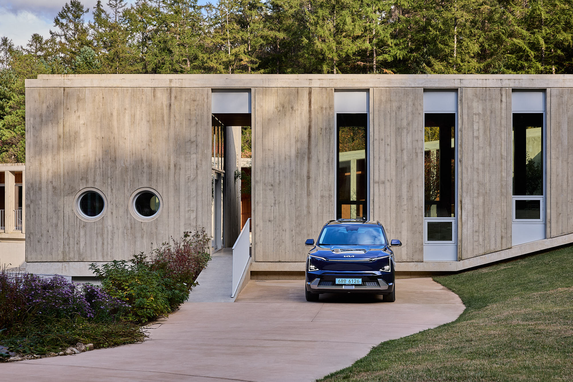 Front view of Kia EV5 framed by Médongaule concrete architecture