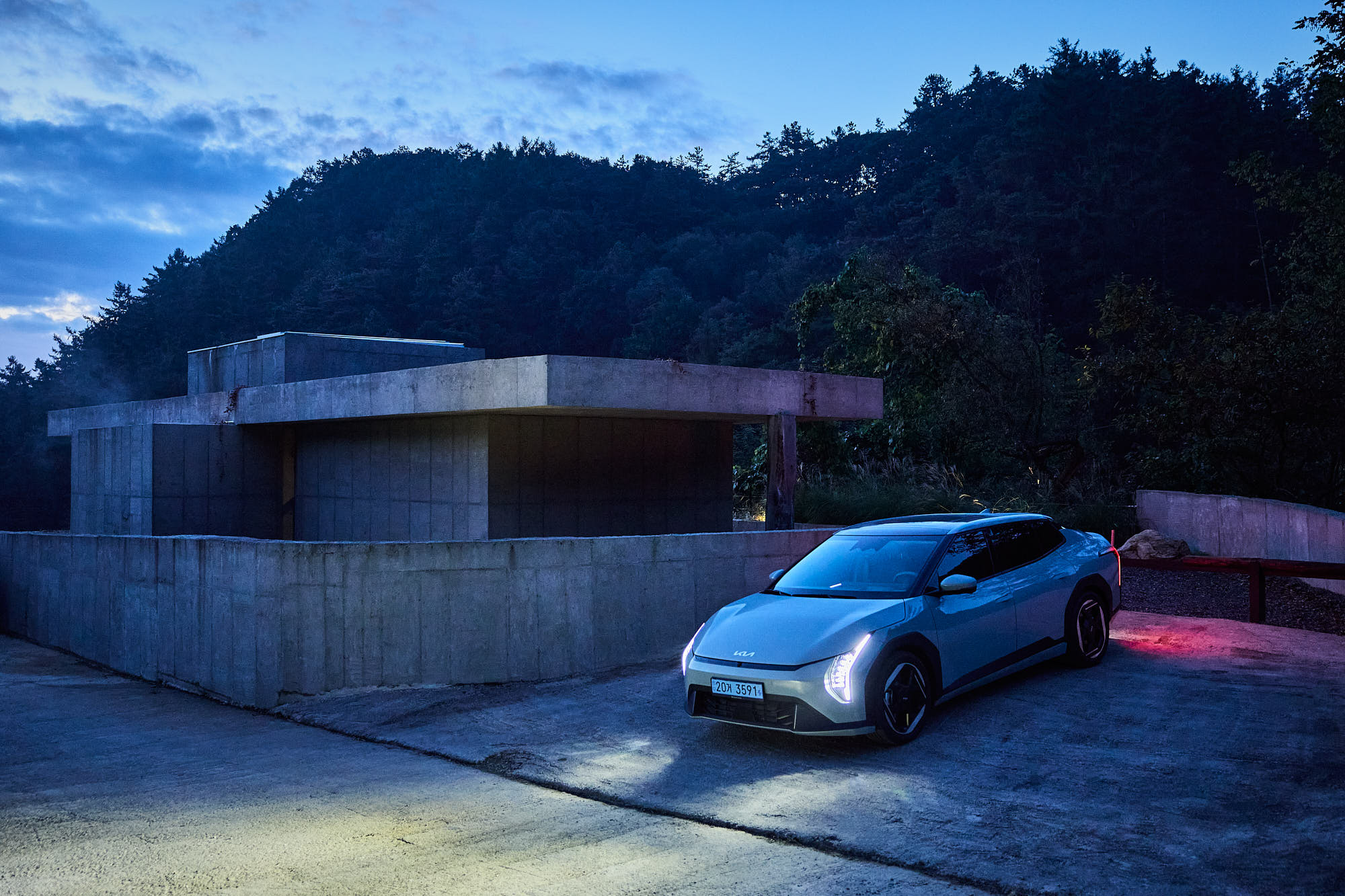 Kia EV4 framed by Myök concrete architecture and forest at blue hour