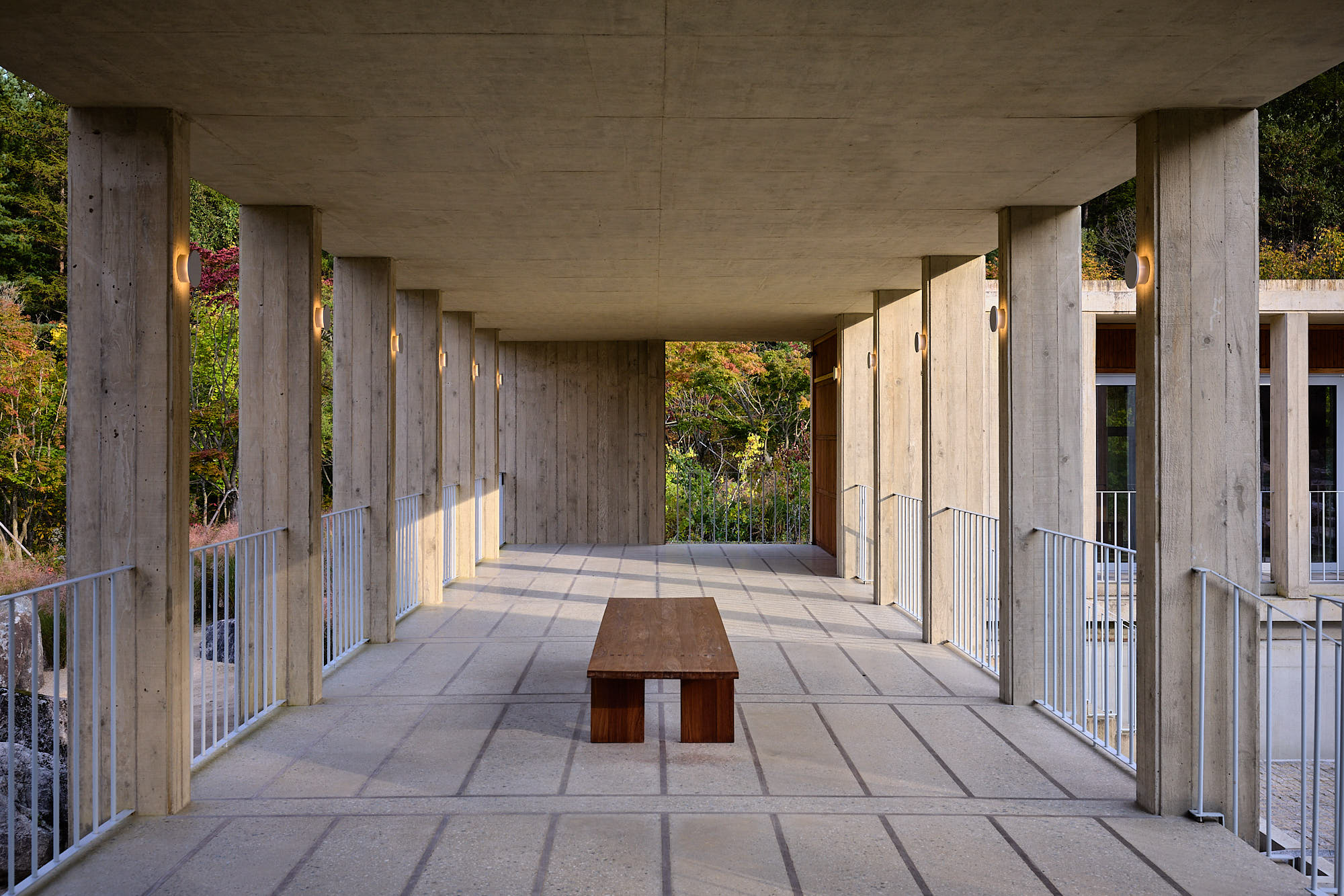 Sunlit concrete colonnade and wooden bench at Médongaule