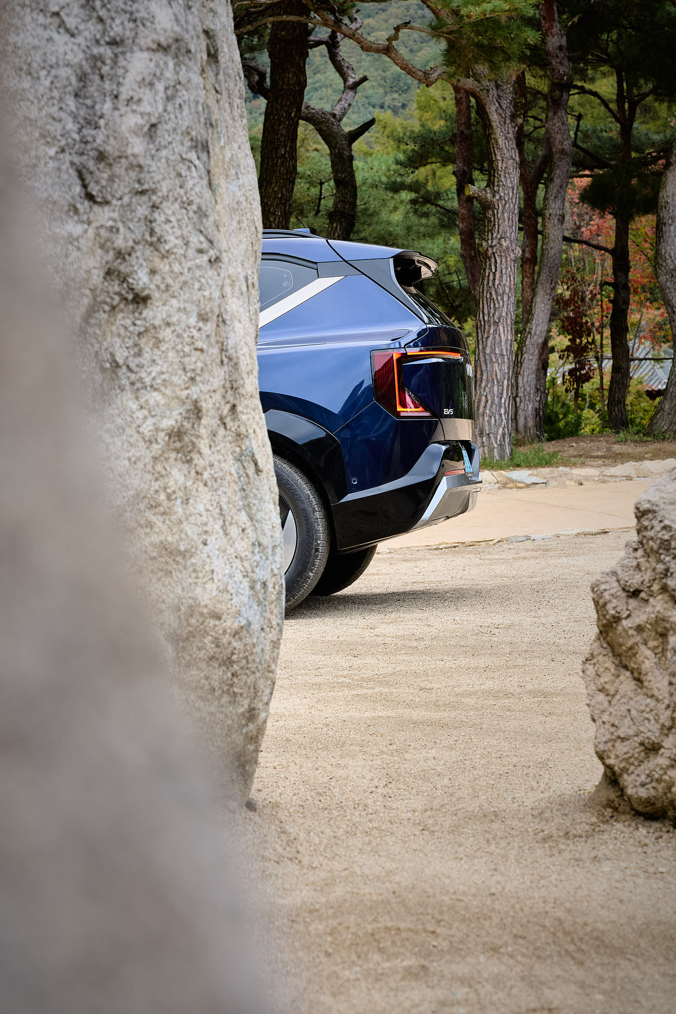 Kia EV5 rear design framed by stone and pine trees at Médongaule