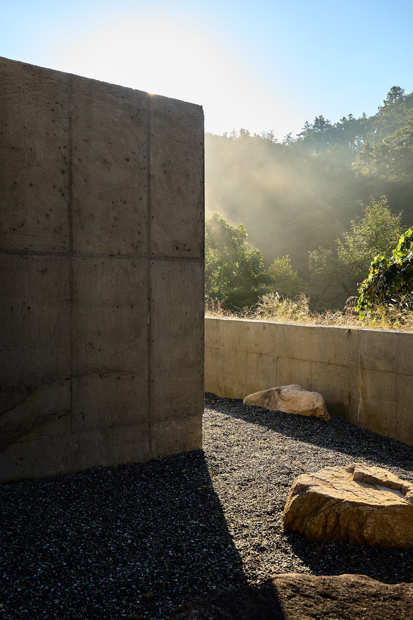 Sunlit concrete walls and stone garden at Myök bathhouse