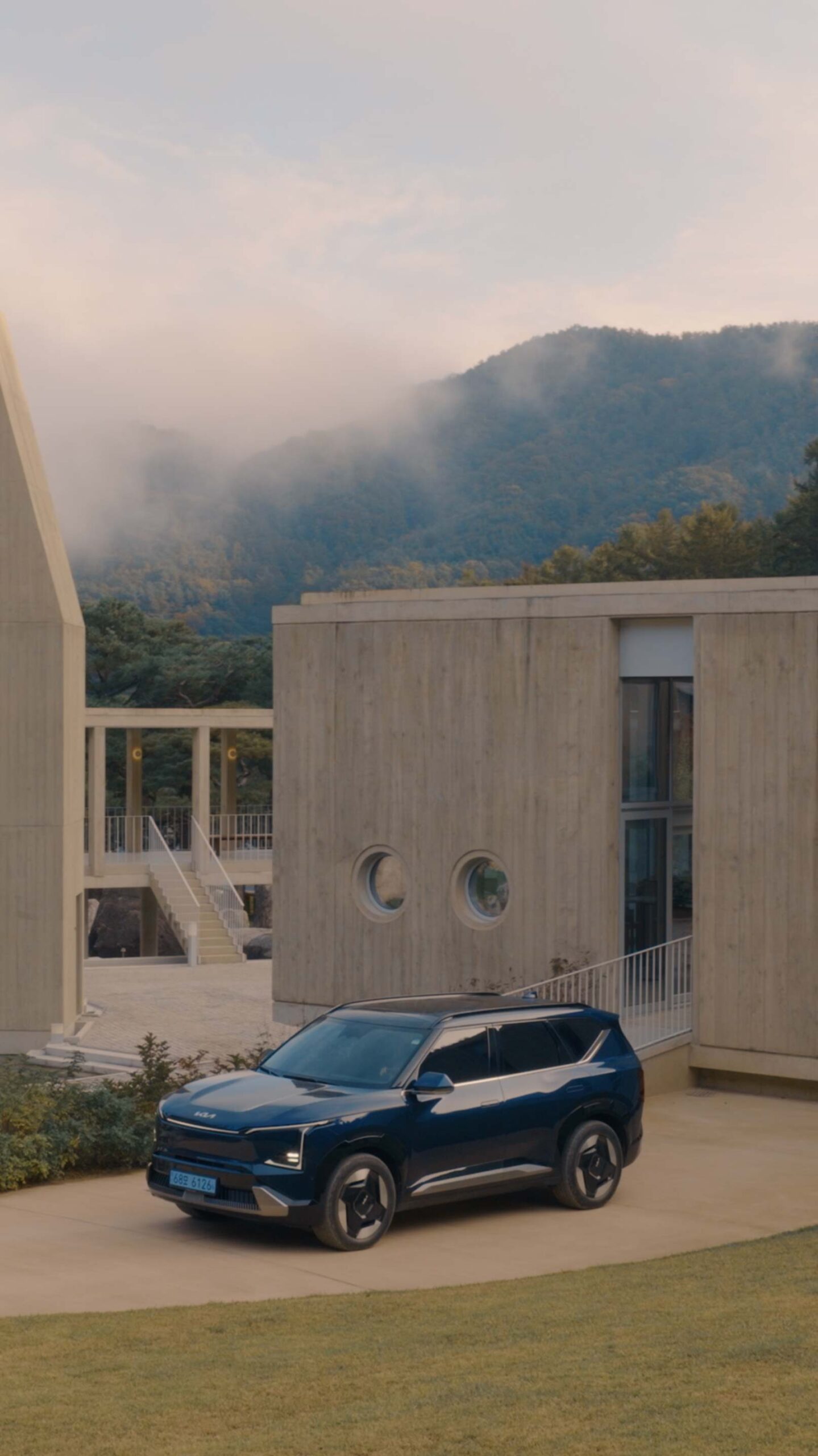 Kia EV5 framed by Médongaule concrete architecture and misty mountains