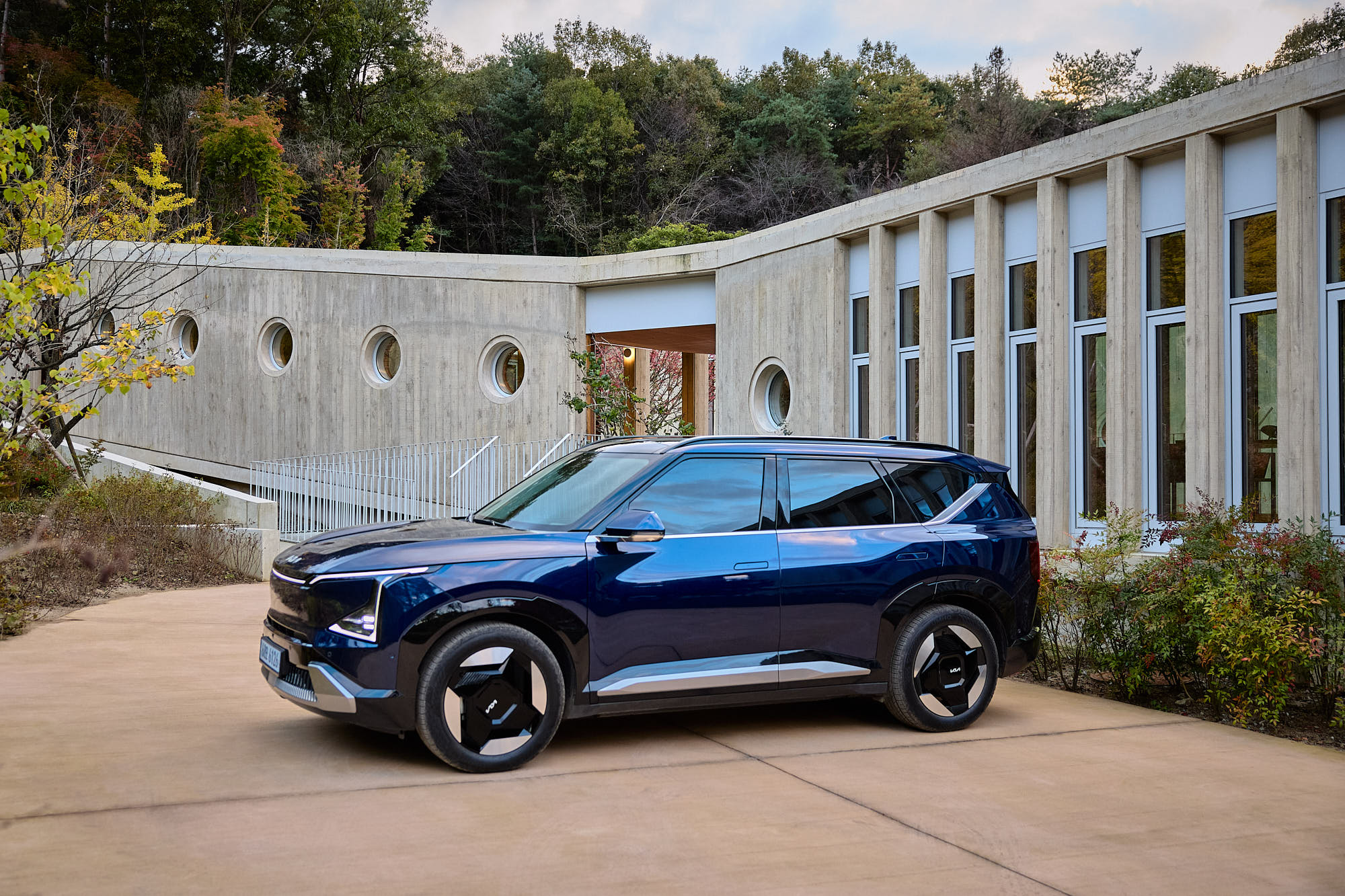 Kia EV5 side profile framed by Médongaule architecture and autumn landscape