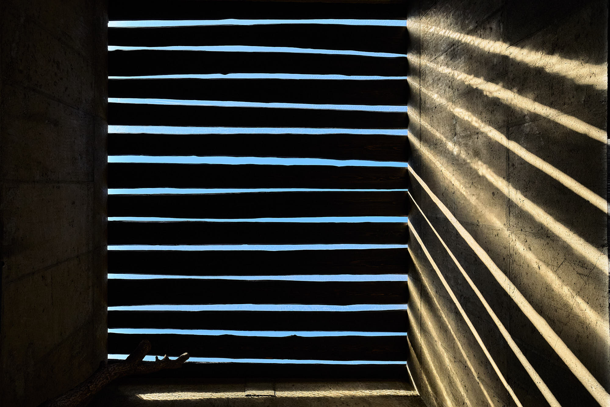 Linear shadows from timber beams across concrete walls at Myök