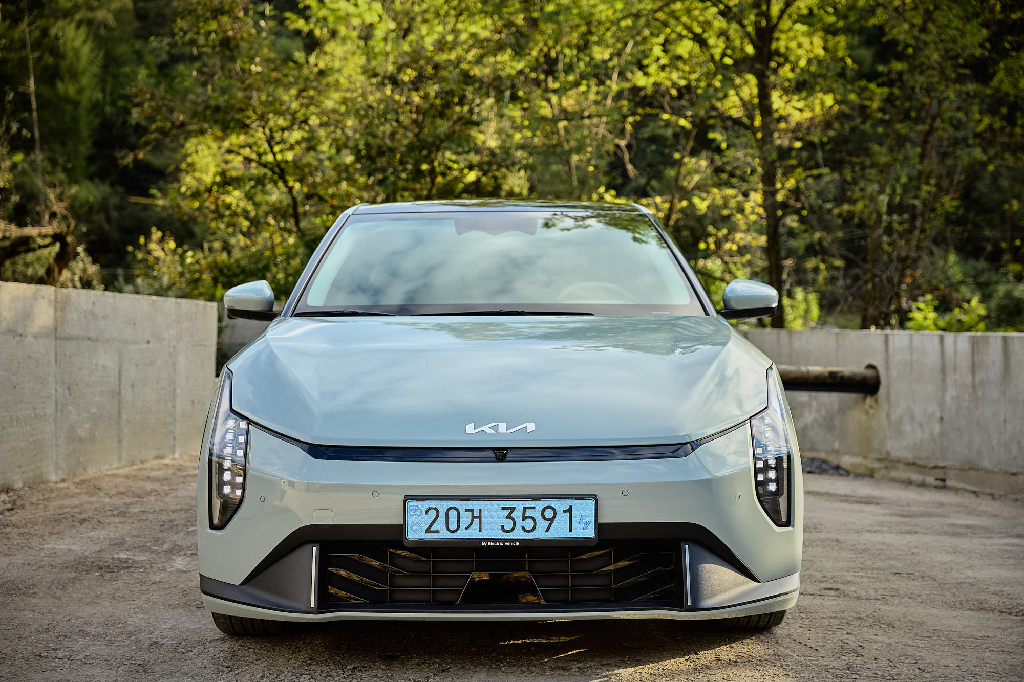 Front view of Kia EV4 beside Myök concrete architecture and forest