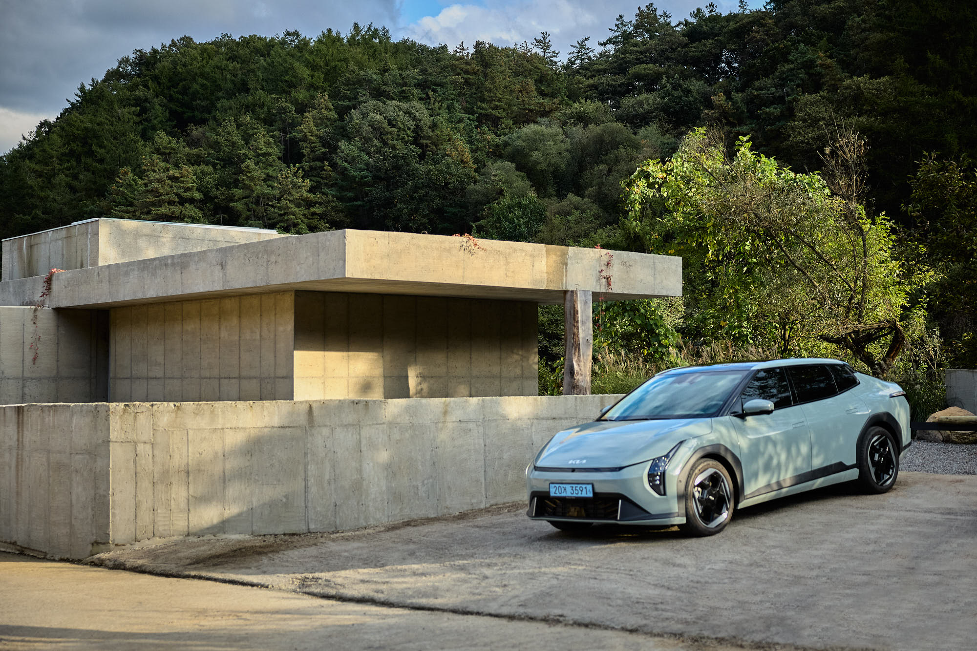 Kia EV4 beside Myök concrete architecture surrounded by forest